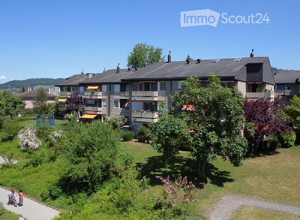 Multi-story residential building with balconies, surrounded by greenery and trees.