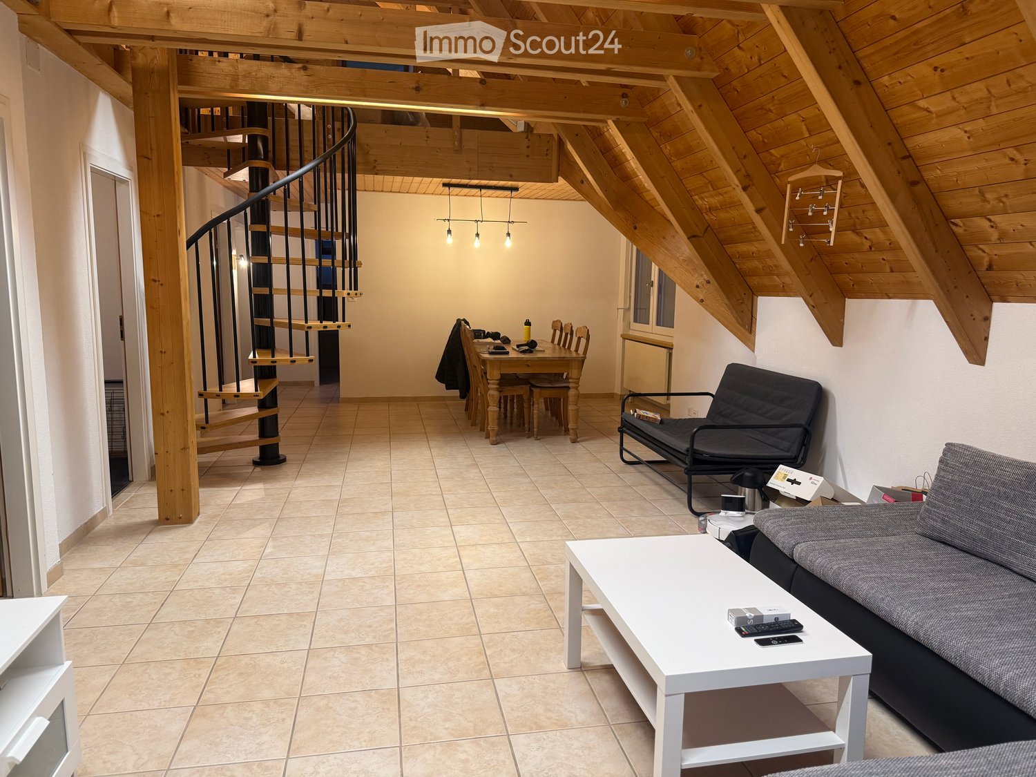 Modern living room with exposed wooden beams, a spiral staircase, a sofa, a coffee table, a dining table with chairs, and a futon.
