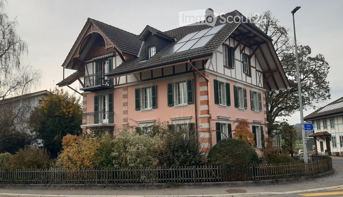 Two-story house with pink facade, green shutters, multiple balconies, and a solar panel on the roof.