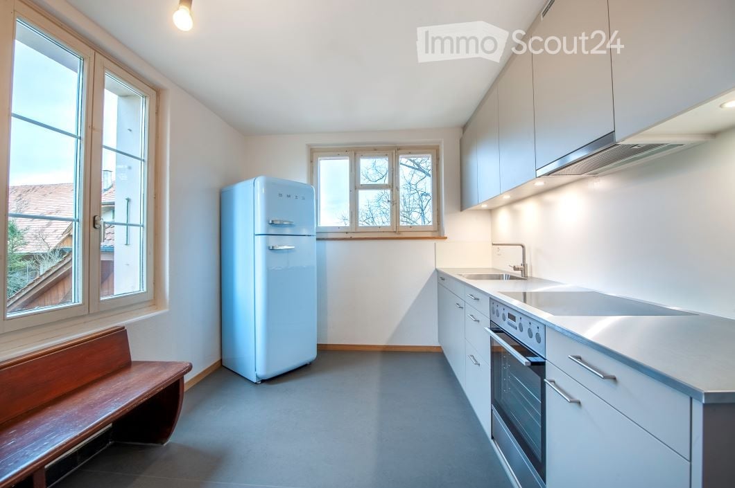 Modern kitchen with white cabinets, stainless steel appliances, a light blue refrigerator, and a wooden bench near the window.