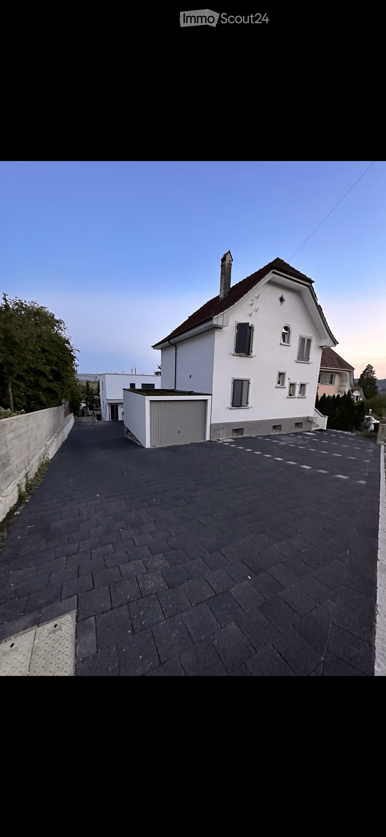 Two-story white house with a red-tiled roof, multiple windows, and a garage attached to the driveway.