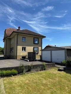 Two-story house with a red-tiled roof, white garage, and a small garden area.