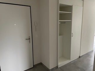 Empty room with white walls, tiled floor, and built-in closet with empty shelves and hanging space.