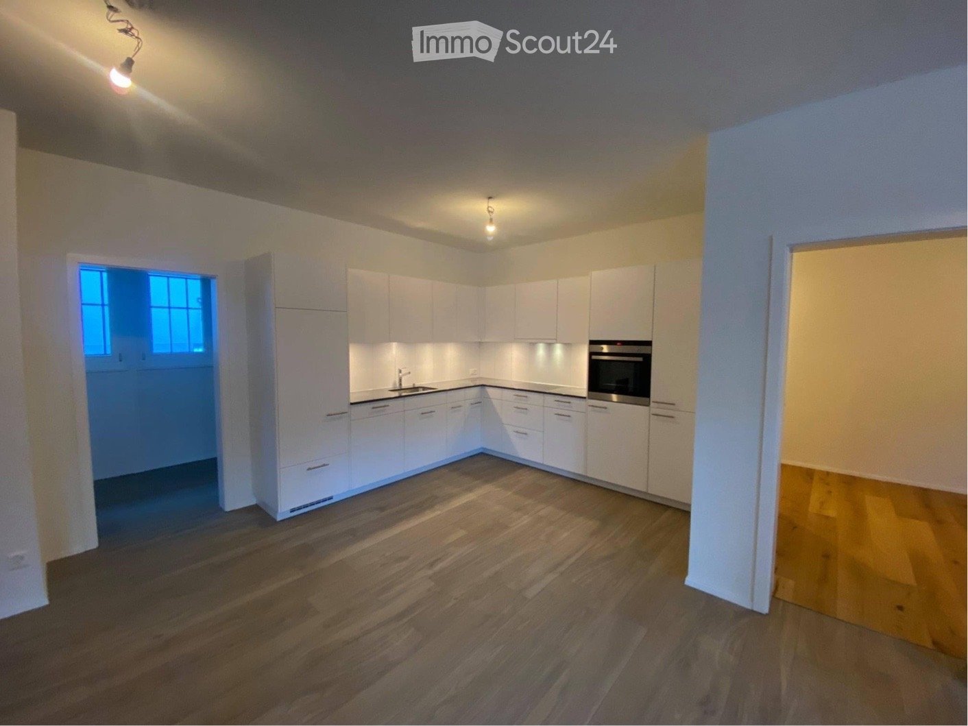 Empty kitchen with white cabinets, wooden flooring, and a built-in oven. No furniture or appliances are present.
