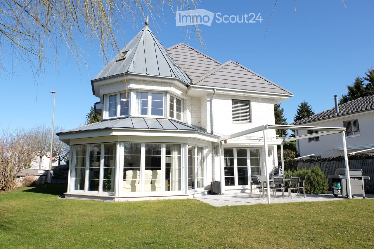 Two-story white house with grey roof, large windows, and a covered patio area with outdoor furniture.