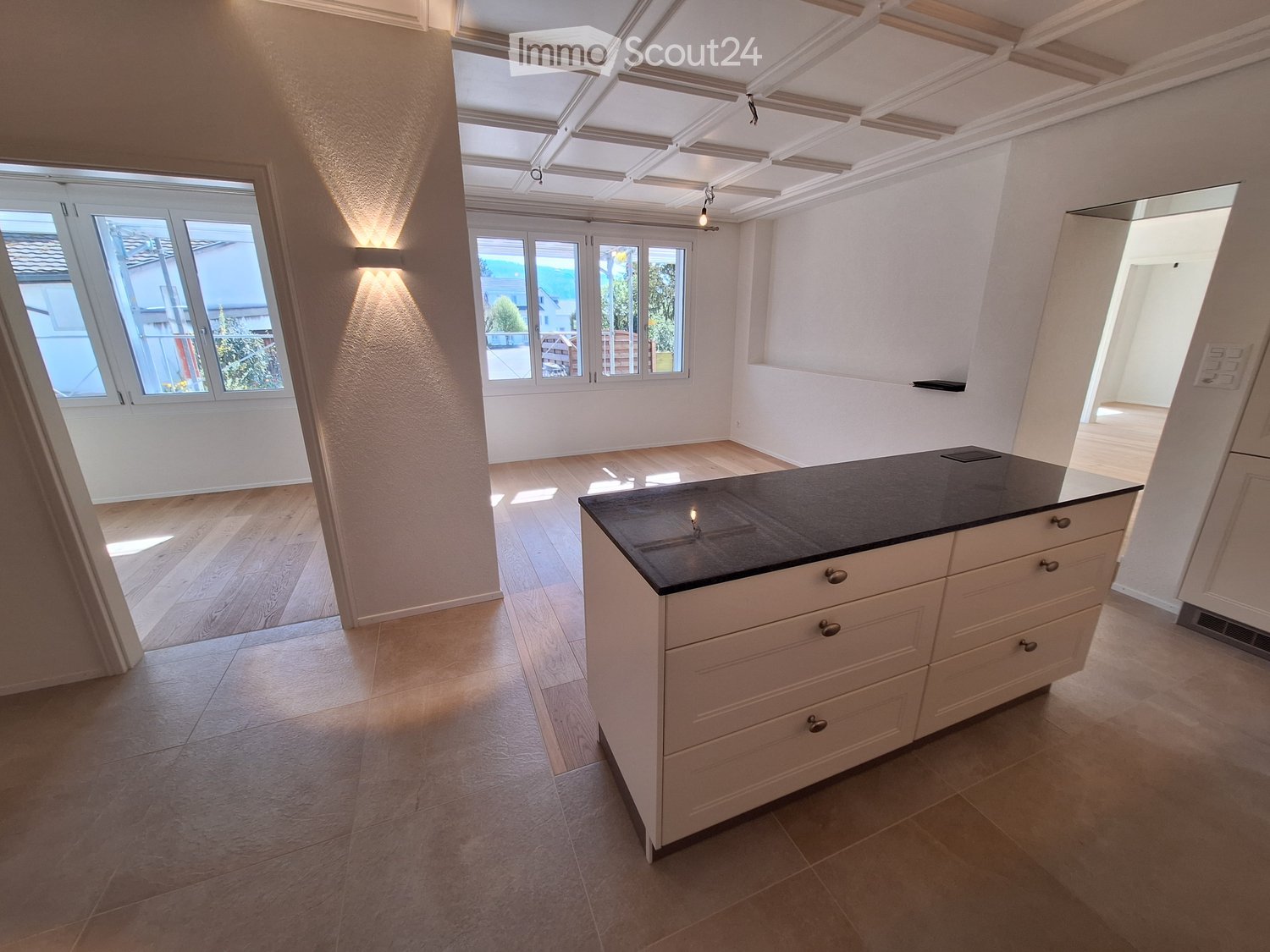 Bright, modern kitchen with a white kitchen island, wooden flooring, and large windows offering natural light and a view of the outdoors.
