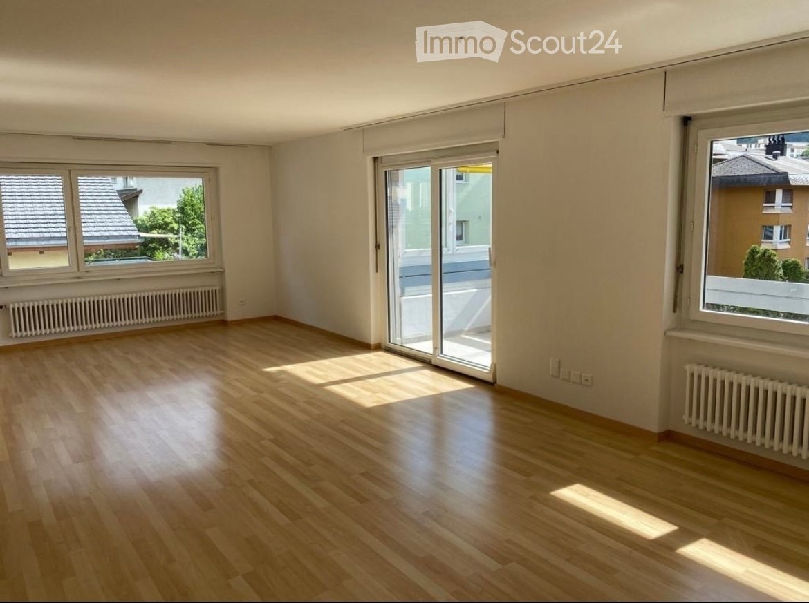 Empty room with wooden flooring, large windows, and a sliding glass door leading to a balcony.