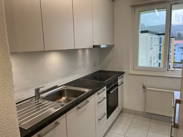 Modern kitchen with white cabinets, stainless steel sink, oven, and a window offering a view of the surrounding area.