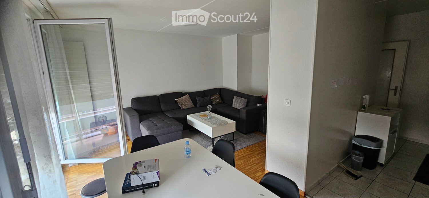 Modern living room with a grey sectional sofa, coffee table, dining table with chairs, and a balcony door with blinds.