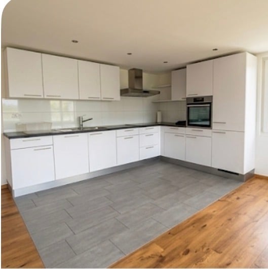 Modern kitchen with white cabinets, stainless steel appliances, and a grey tiled floor. Features include a sink with a modern faucet, an oven, and a range hood.