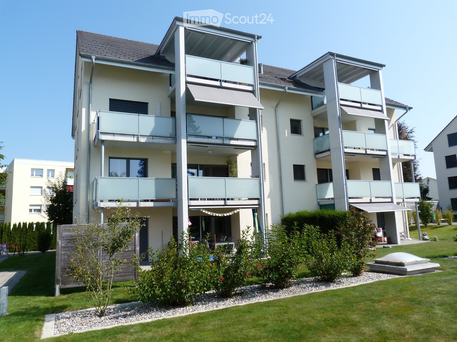 Building. Modern multi-story residential building with balconies, large windows, and surrounding greenery.
