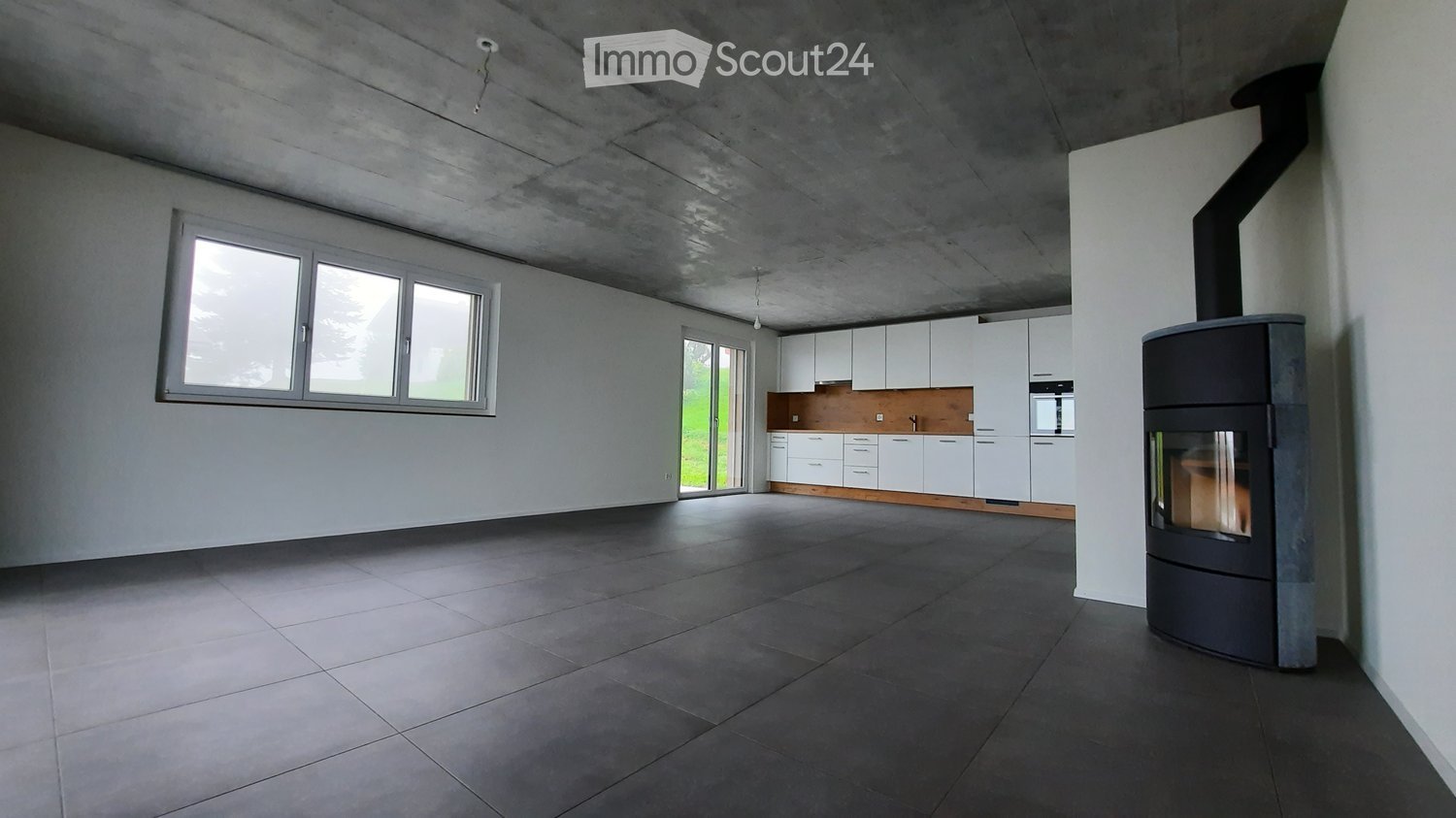 Modern, minimalist kitchen area with white cabinets, dark tiled floor, large windows, and a contemporary fireplace.