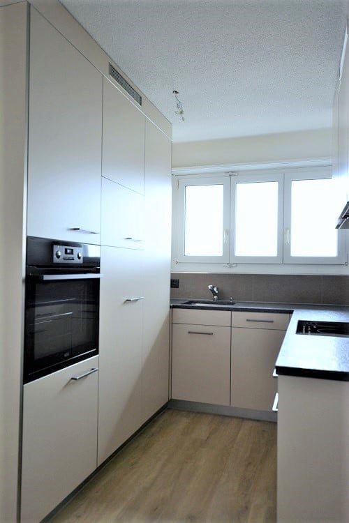 Modern kitchen with white cabinets, wooden flooring, built-in oven, and a sink with a faucet.