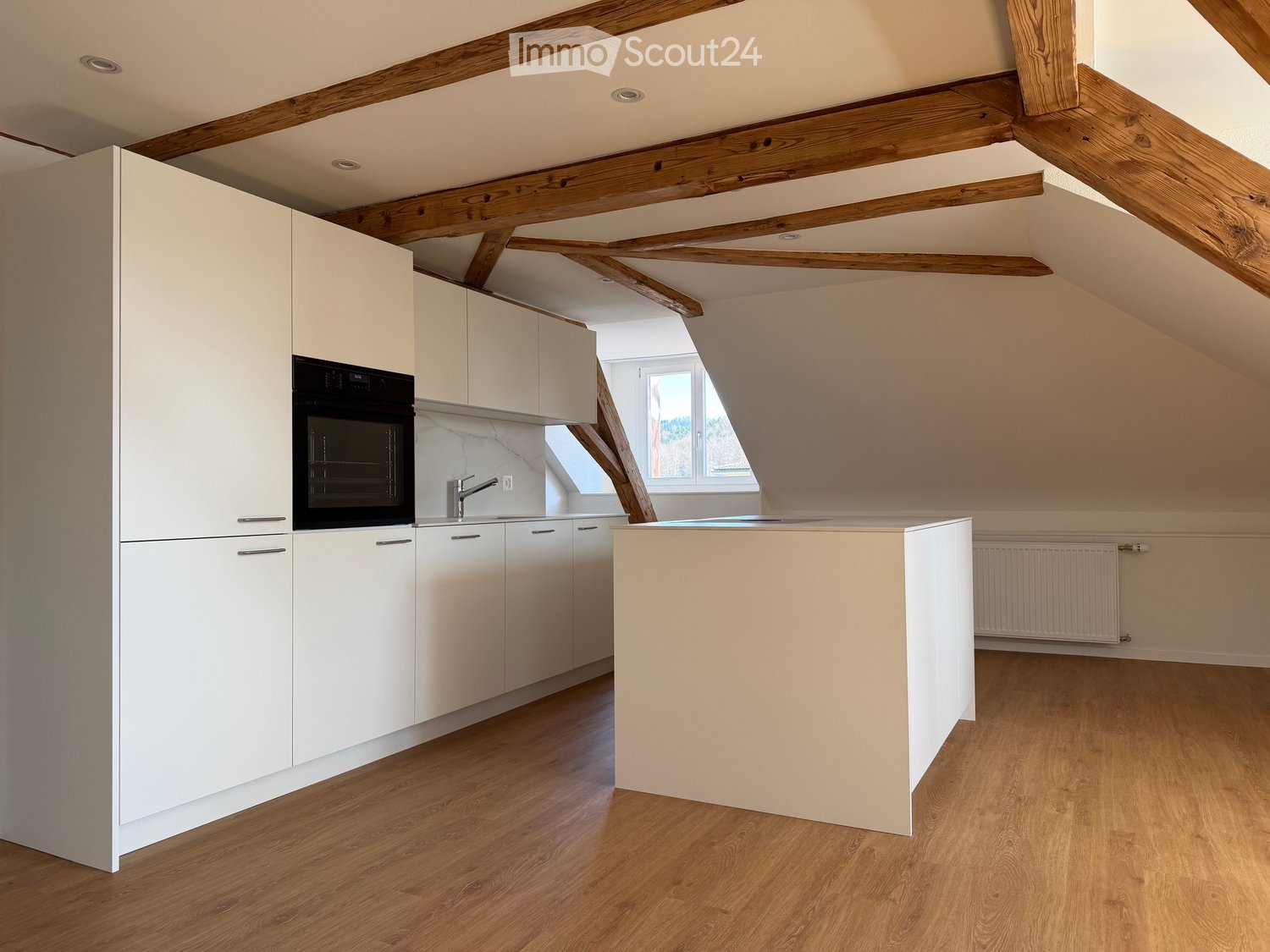Modern kitchen with white cabinets, a central island, and an integrated oven. The space features wooden flooring and exposed wooden beams on the ceiling.