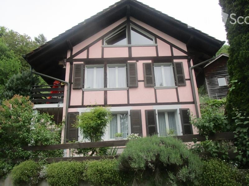 Pink and white half-timbered house with multiple windows, shutters, and a small balcony on the upper floor.