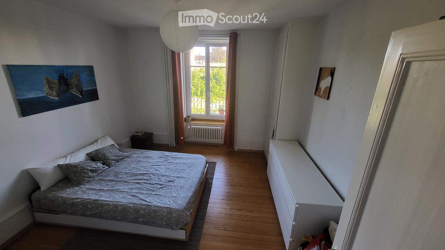 Cozy bedroom with a bed, nightstand, drawer, picture frame, and radiator near the window.