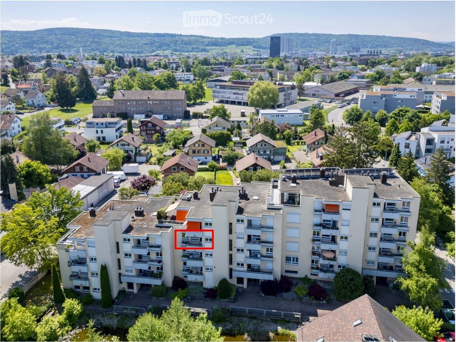 Aerial view of a multi-story residential building surrounded by greenery and other houses in a suburban neighborhood.
