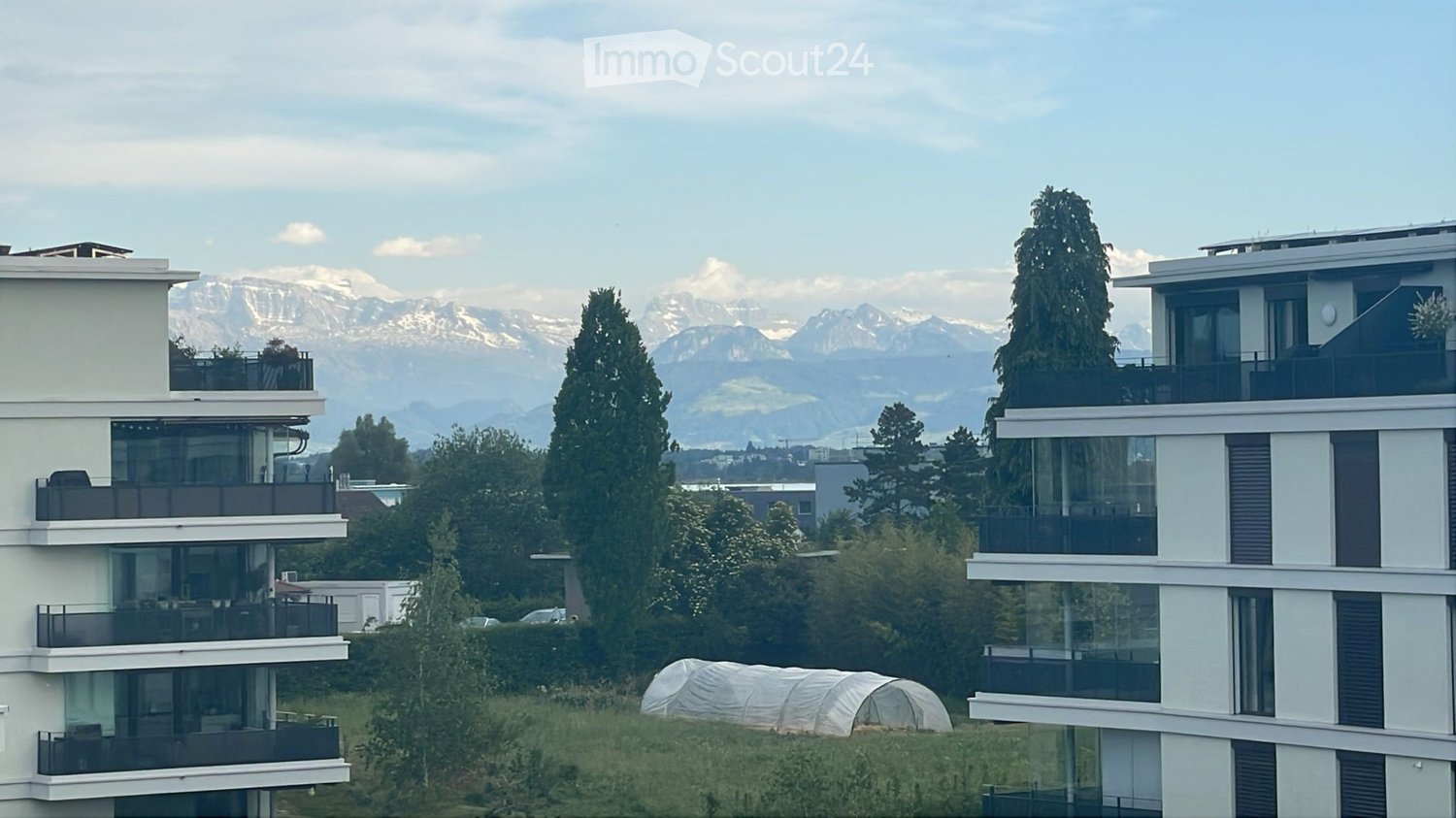 Modern multi-story residential building with balconies and large windows, overlooking a scenic mountain range.