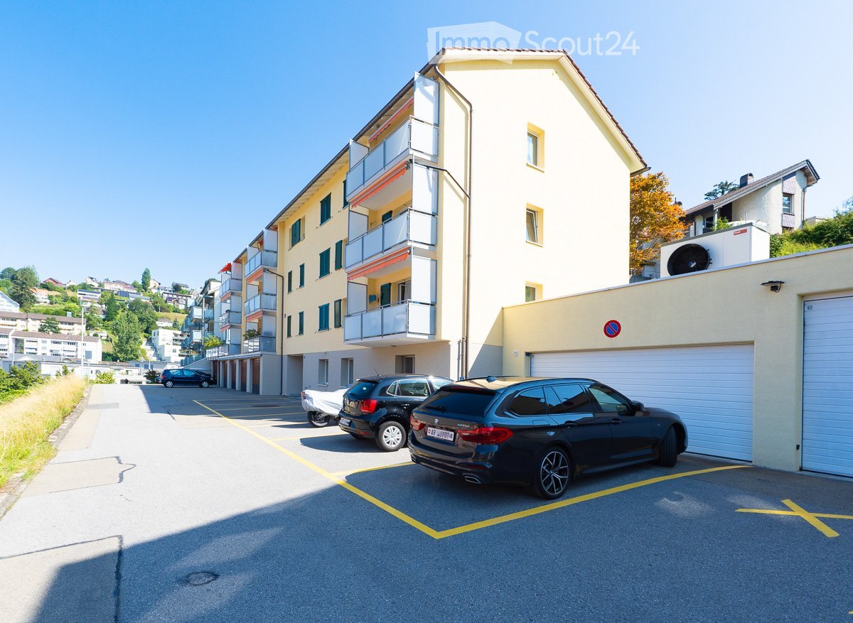 Multi-story residential building with balconies, garage, and several parked cars in the parking area.