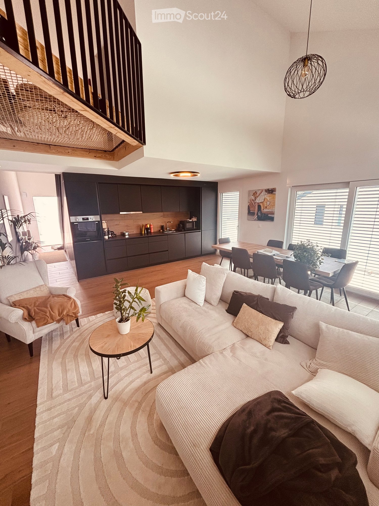 Modern open-plan living and dining area with a white sofa, coffee table, dining table with chairs, and a kitchen area with dark cabinets and appliances.