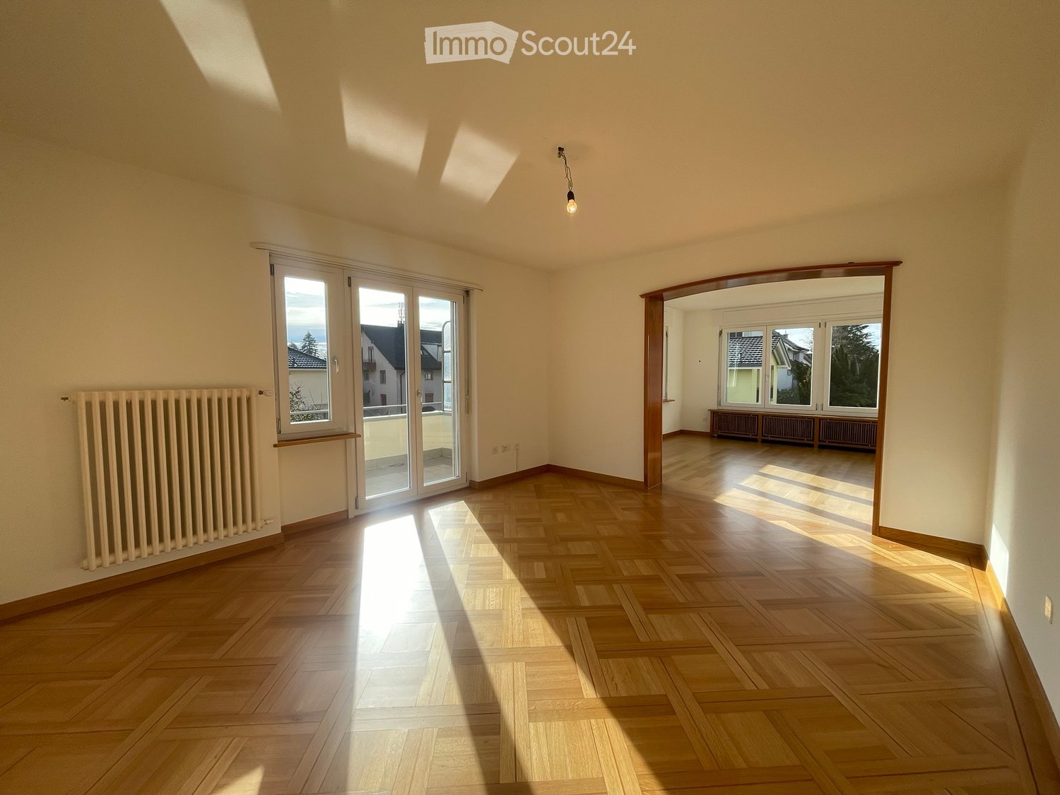 Empty room with wooden flooring, large windows, and radiators. No furniture or equipment present.