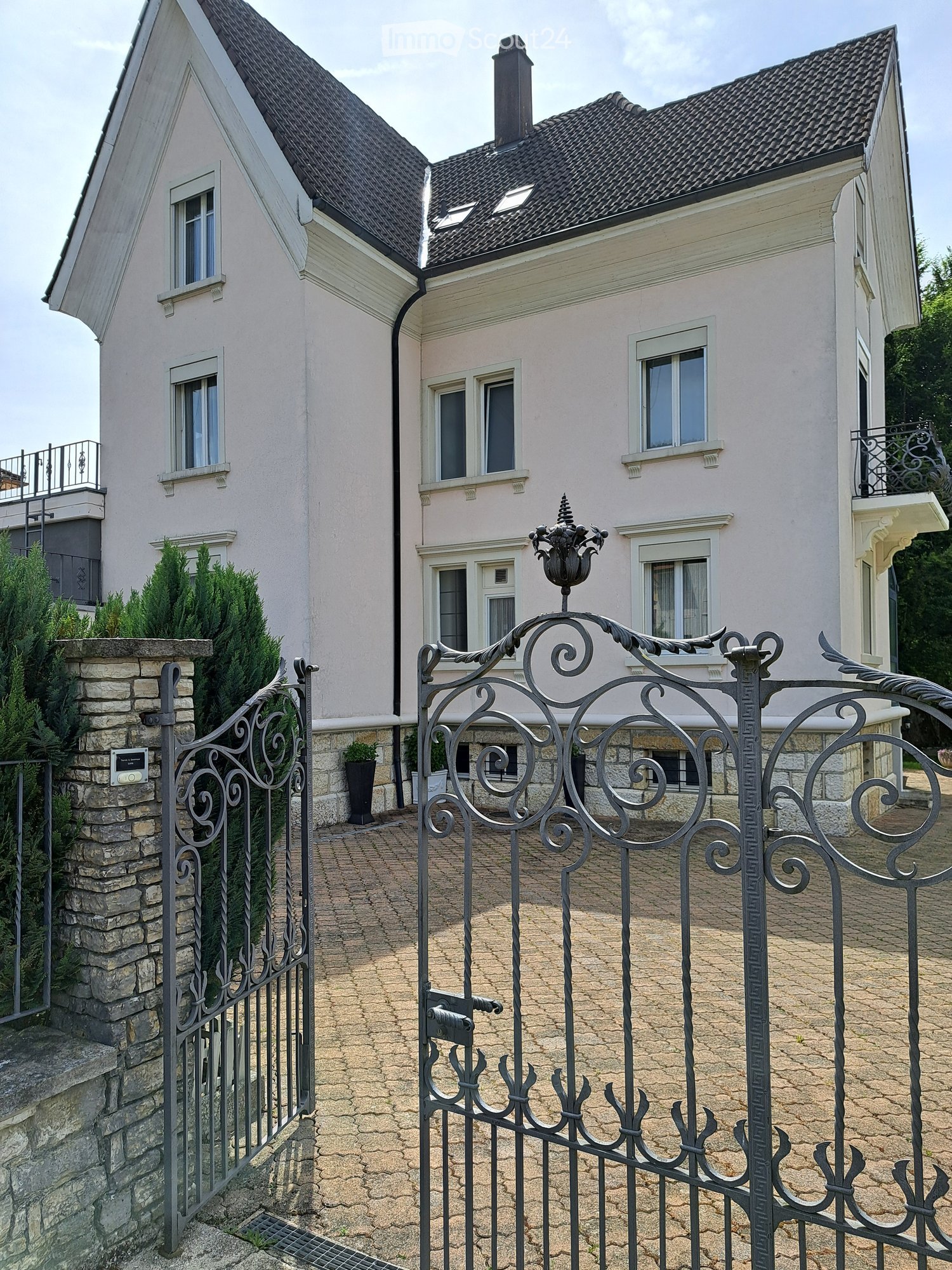 Two-story house with light pink exterior, multiple windows, and ornate metal gate.