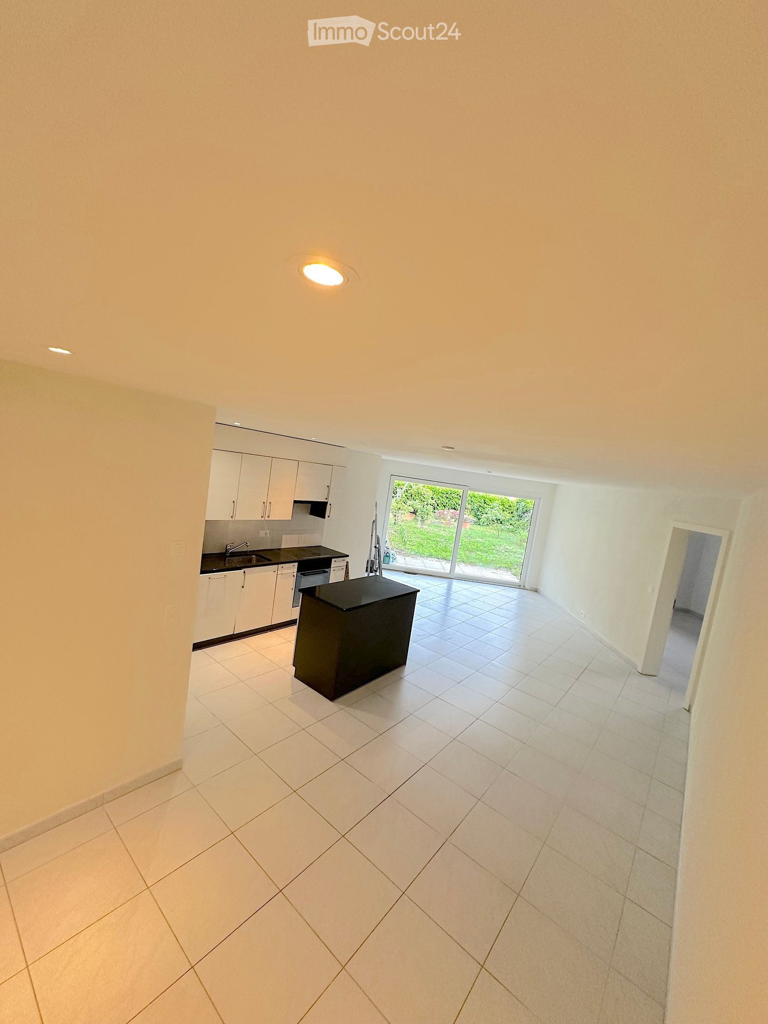 Modern kitchen with white cabinets, black countertops, and a central island. The space features tiled flooring and large windows overlooking a garden.