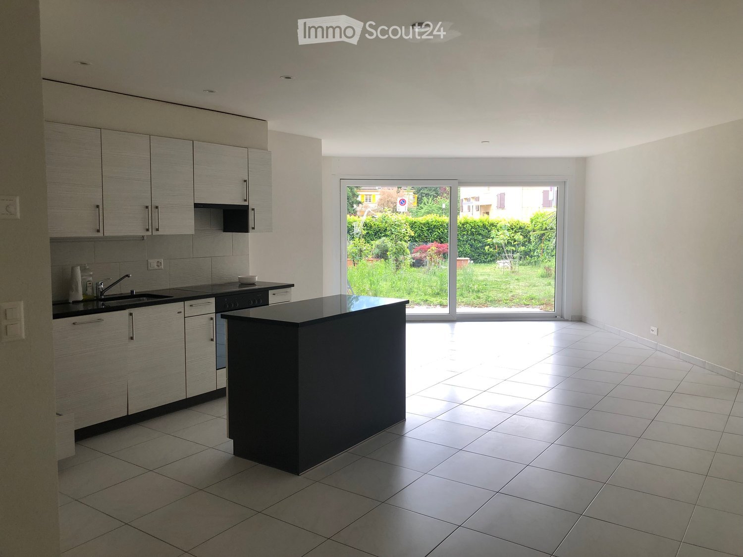 Modern kitchen with light grey cabinets, black countertops, a central island, and a large window overlooking a garden.