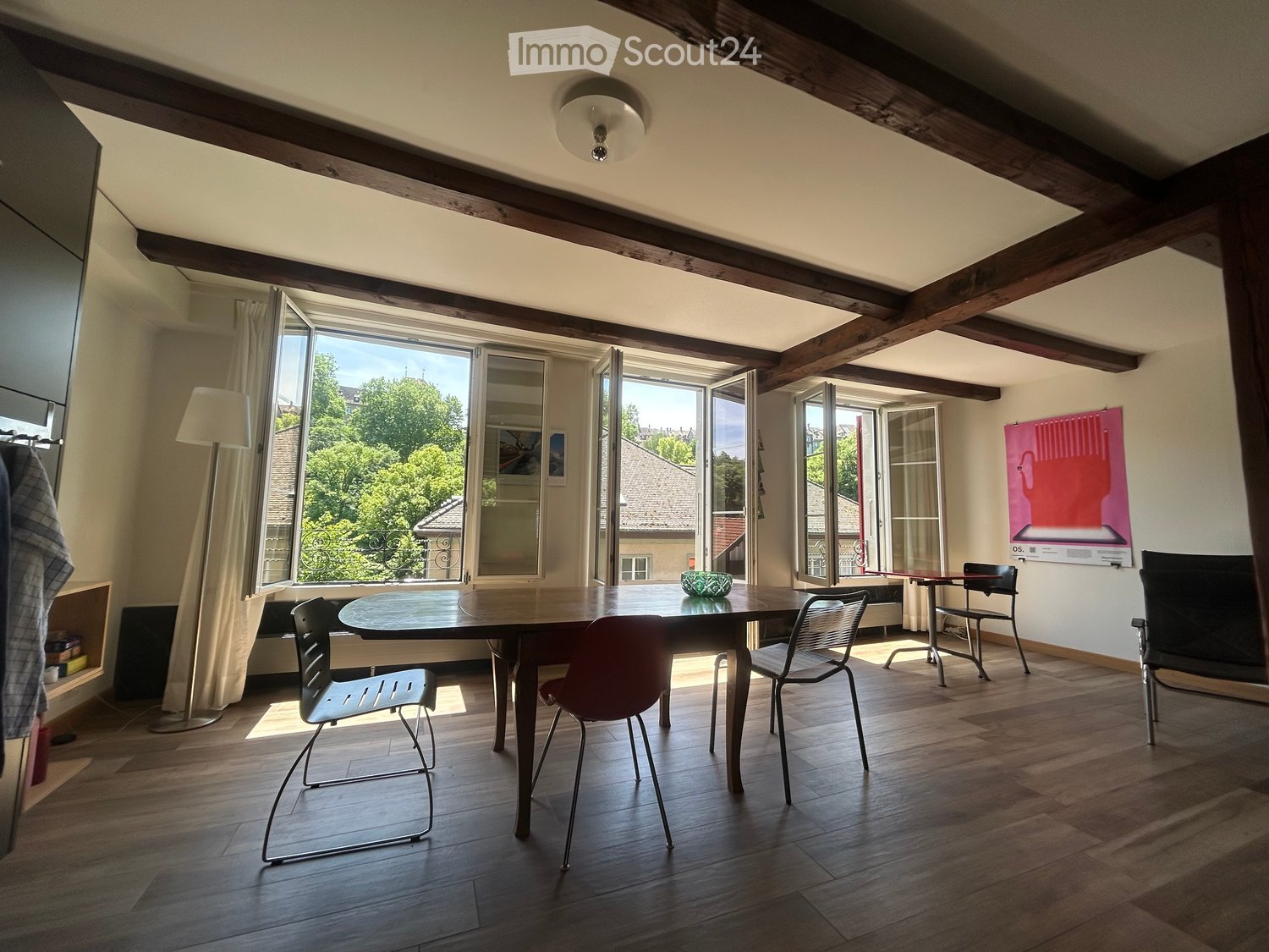 Bright dining area with wooden floor, large windows, exposed wooden beams, and modern chairs around a central table.