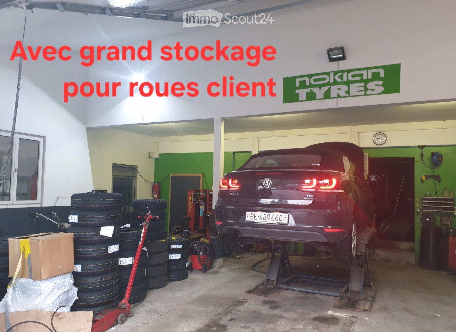 Garage with a car on a lift, stacks of tires, tools, and equipment.
