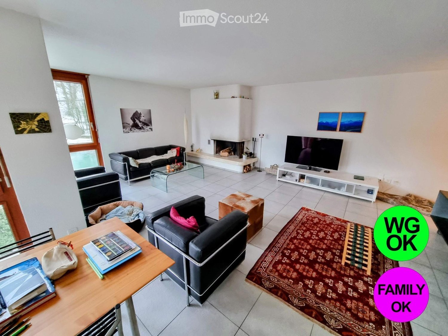 Modern living room with white walls, tiled floor, fireplace, sofa, armchairs, coffee table, TV, and a large area rug.
