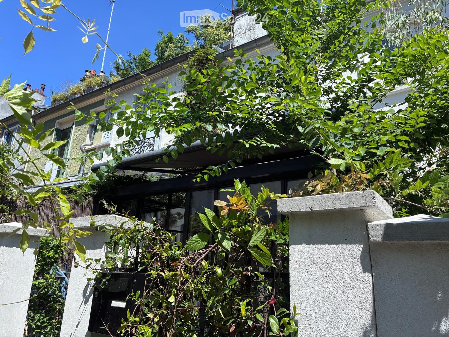 A multi-story residential building with green ivy and climbing plants covering parts of the facade, visible windows, and a rooftop area with greenery.