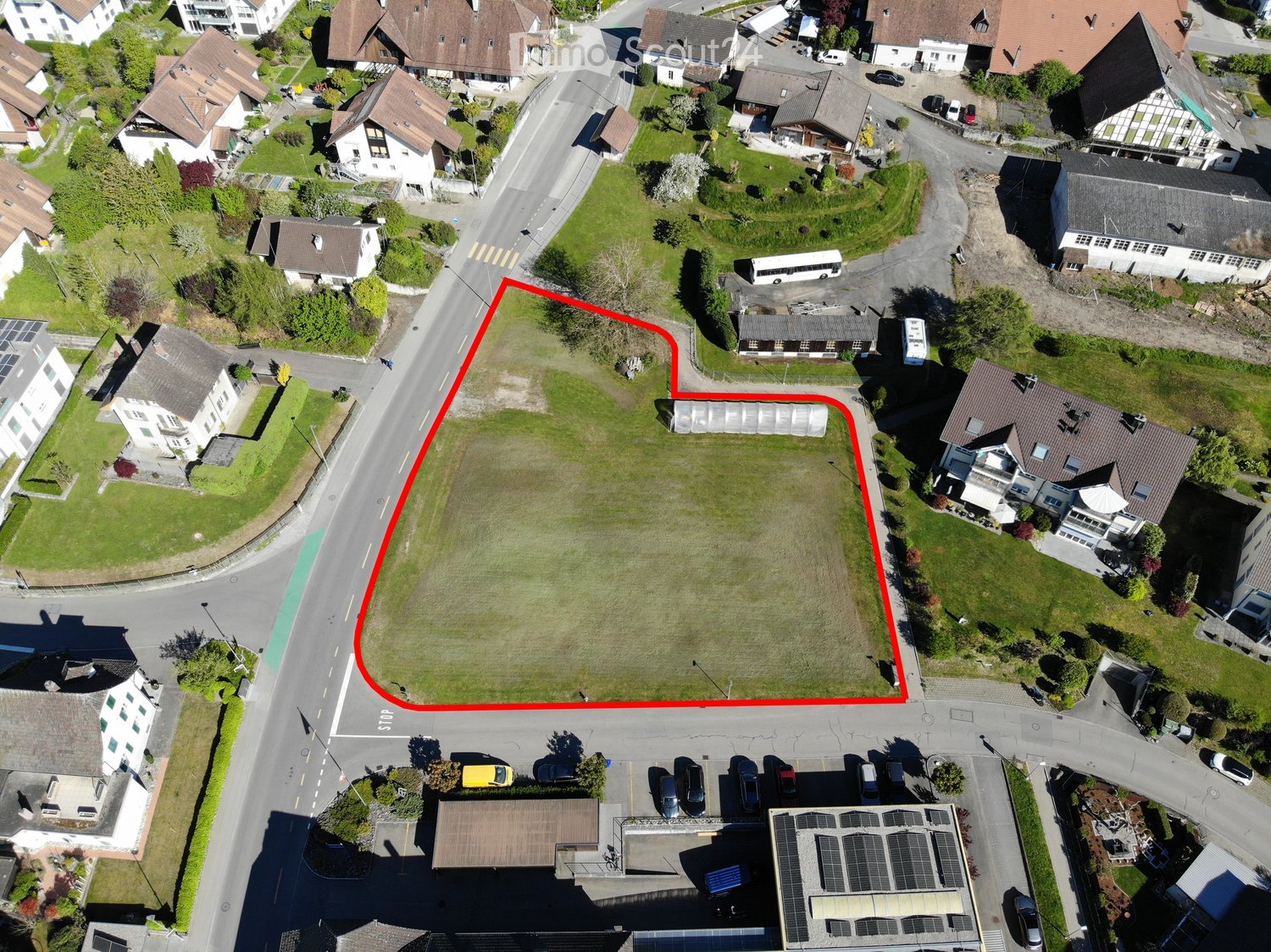 Aerial view of a residential area with multiple houses, green spaces, and a highlighted plot of land outlined in red.
