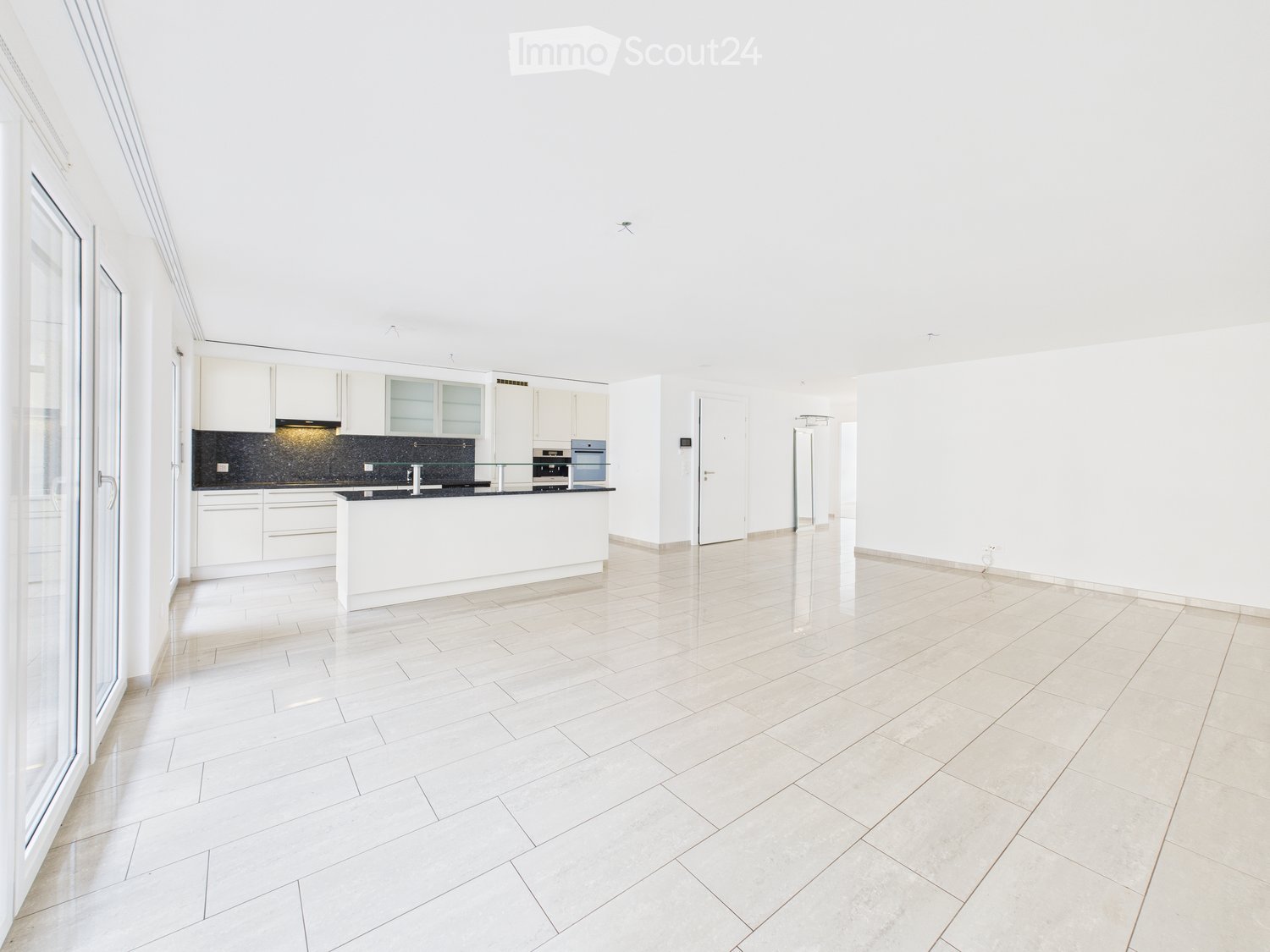 Bright, open-plan living and kitchen area with white tiled flooring, white kitchen cabinets, a central island, and modern appliances.