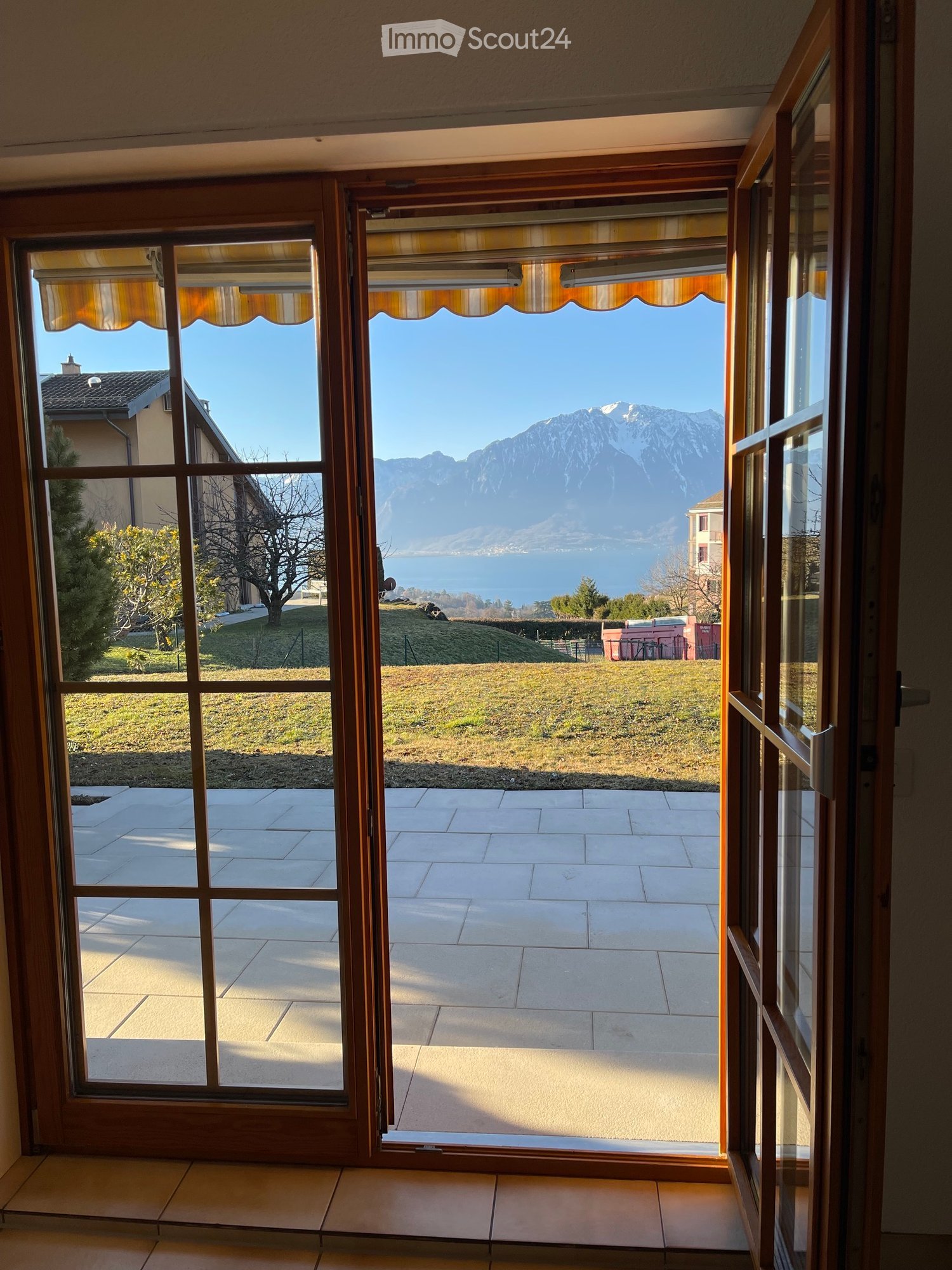 Open sliding glass doors leading to a tiled patio with a scenic view of a lake and mountains.