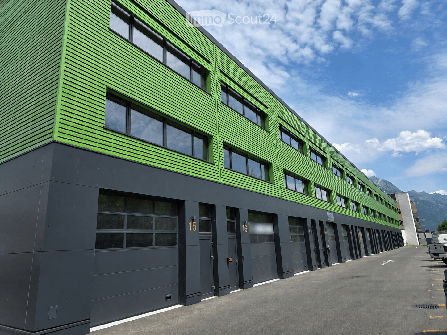 Modern multi-story building with green and black exterior, large windows, and numbered garage doors.