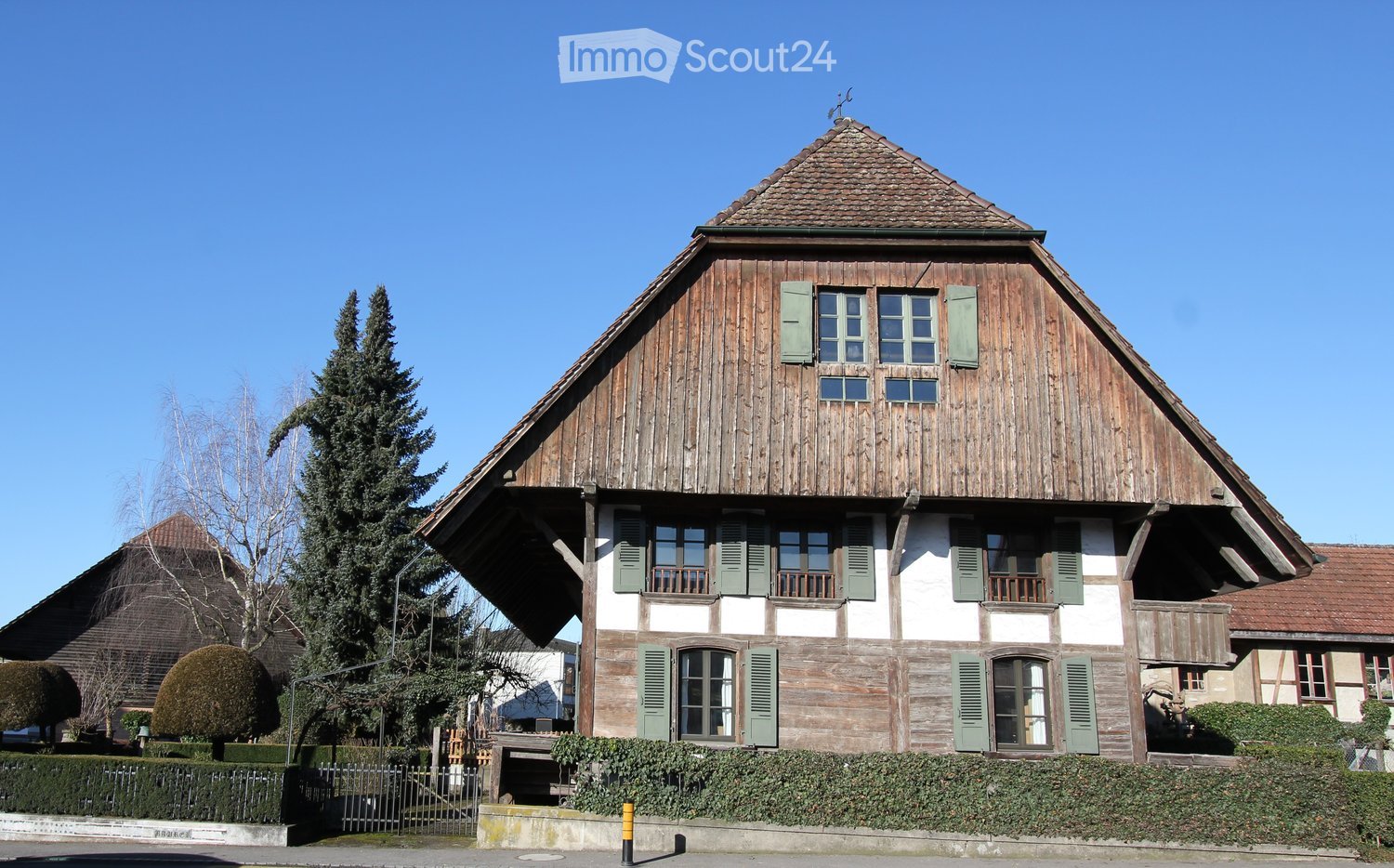 Traditional wooden house with a steep roof, green shutters, and a small garden in front.