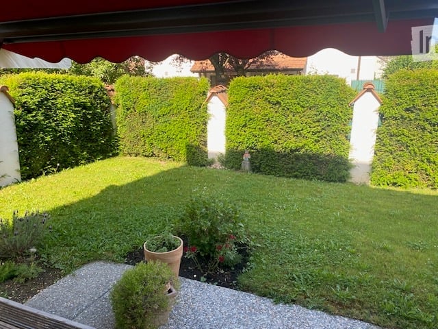 Well-maintained garden with neatly trimmed hedges, a small lawn, and a few potted plants near the entrance.