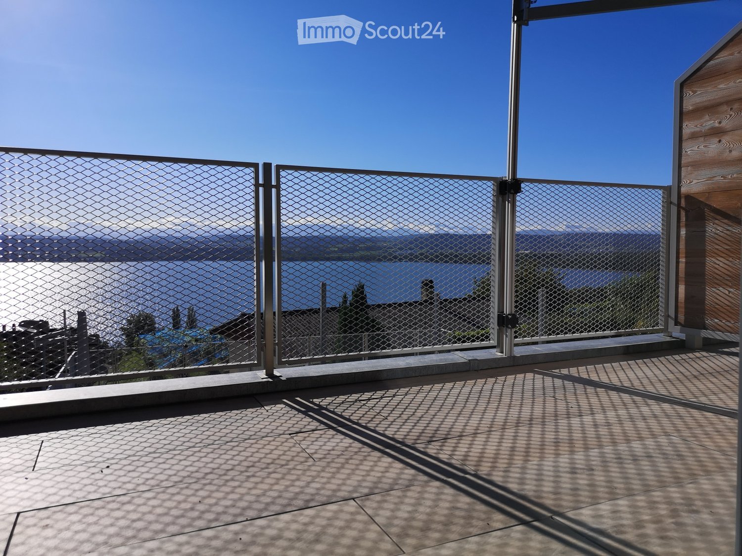 Balcony with metal railing, overlooking a body of water and distant mountains under a clear blue sky.