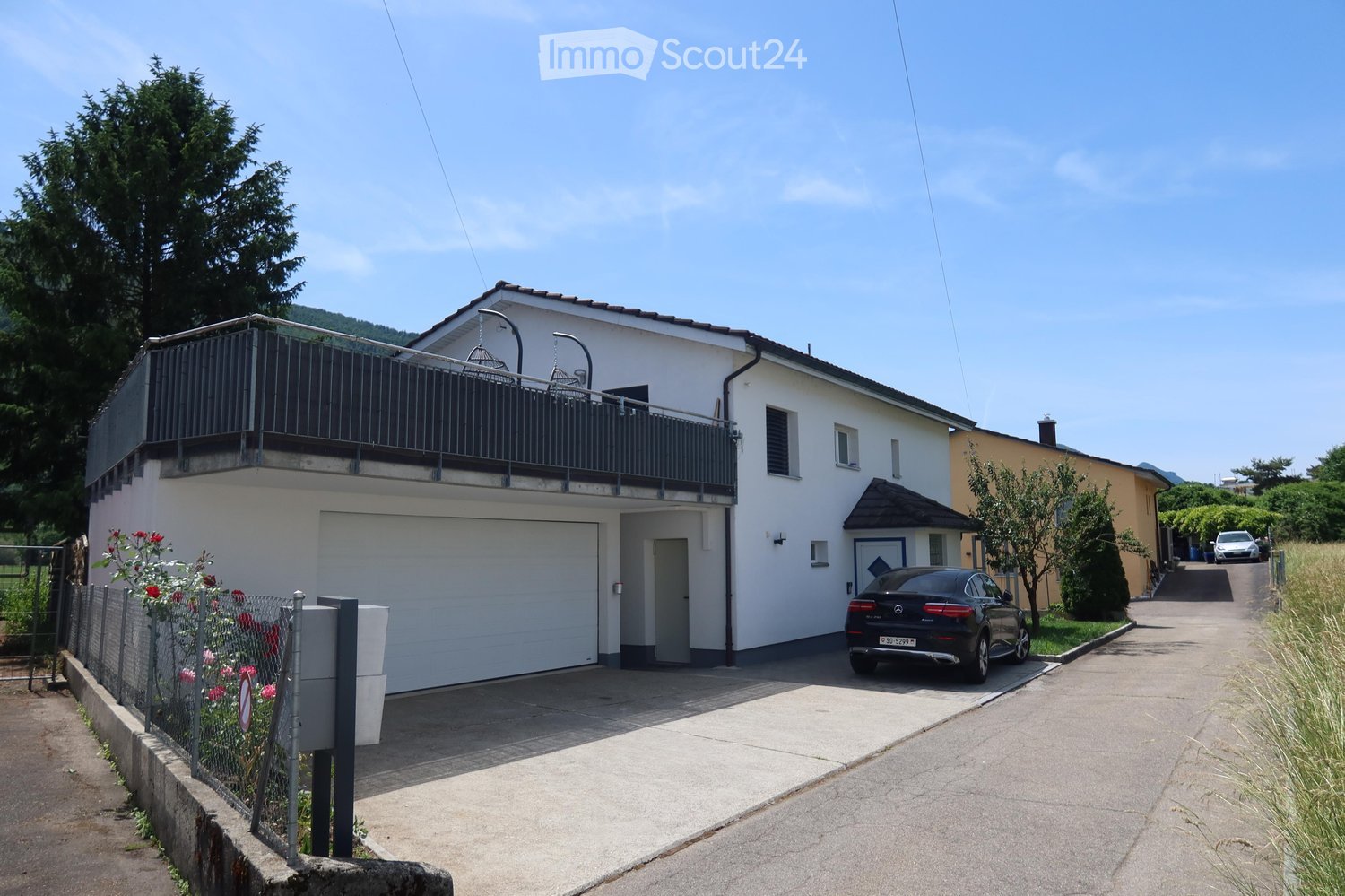 Two-story house with white exterior, garage, balcony, and a parked car in front.