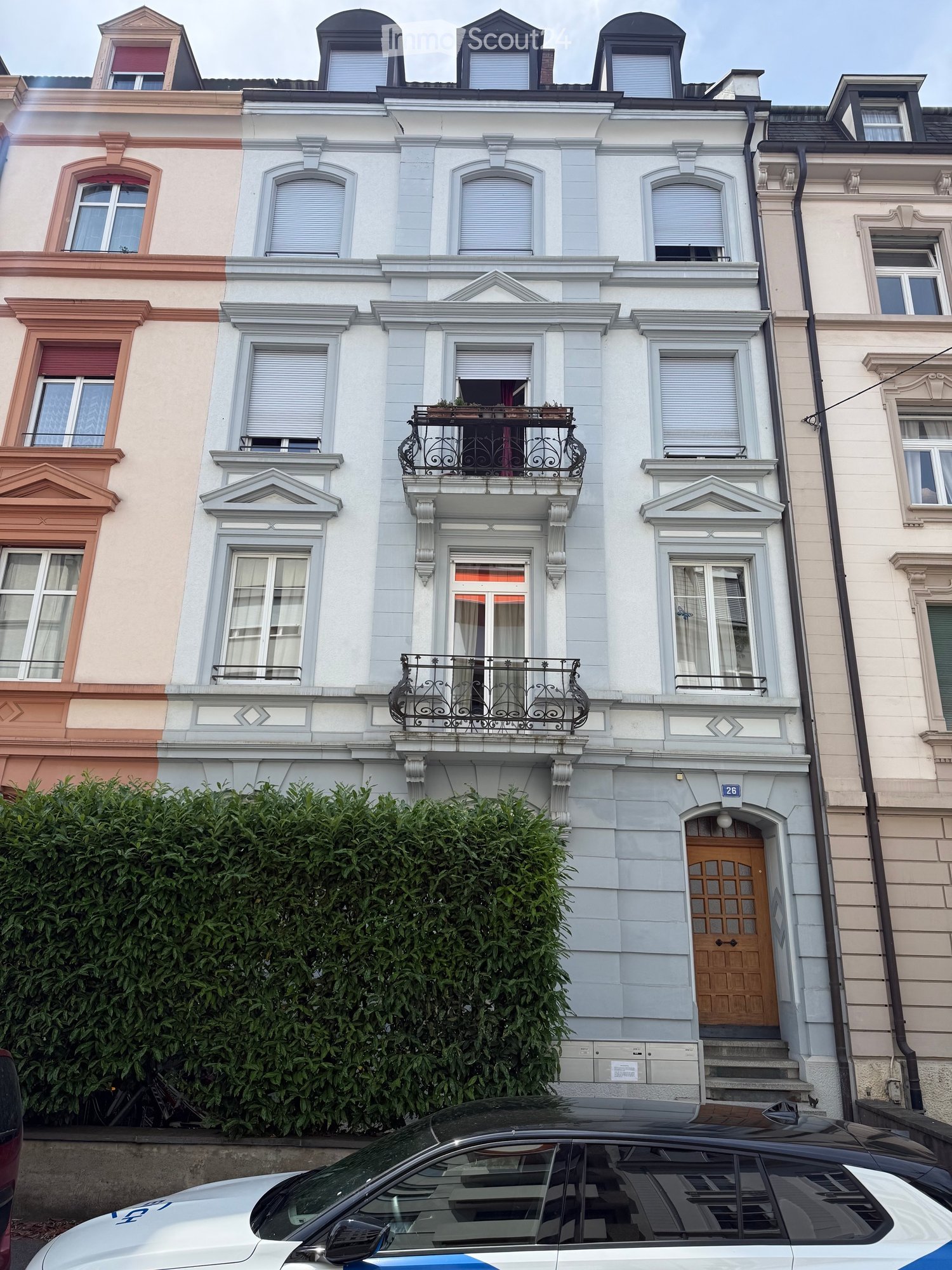 A multi-story residential building with light blue and white facade, ornate balconies, and decorative window frames.