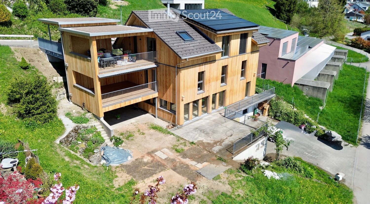 2 story house, wooden exterior, solar panels on the roof, raised ground floor, balcony, driveway, garden