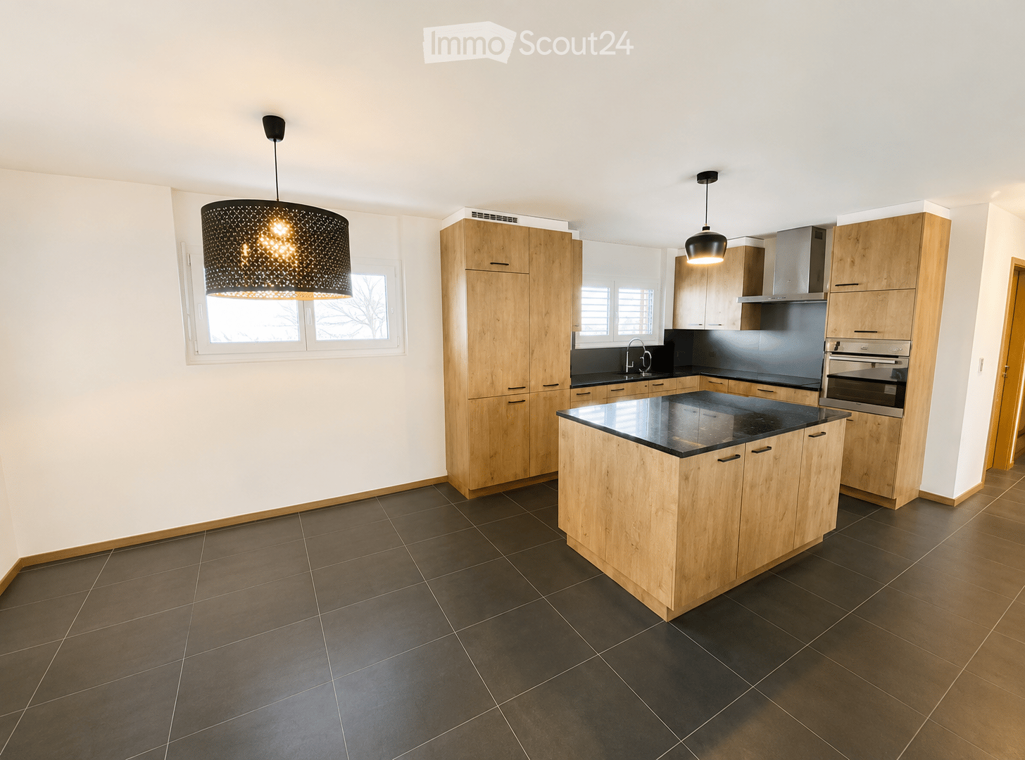Modern kitchen with wooden cabinets, black countertops, and a central island. Features pendant lighting and stainless steel appliances.