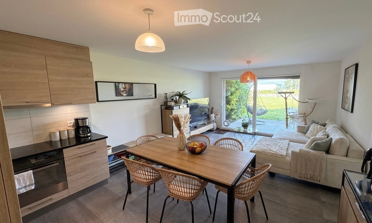 Open-plan living and dining area with modern furniture, a kitchen area, and a view of a garden through large windows.