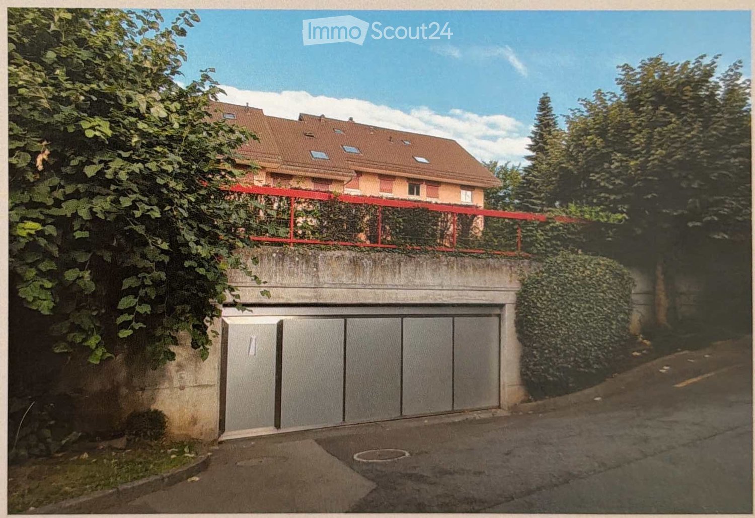 A multi-story residential building with a large garage entrance, surrounded by greenery and a raised ground floor.
