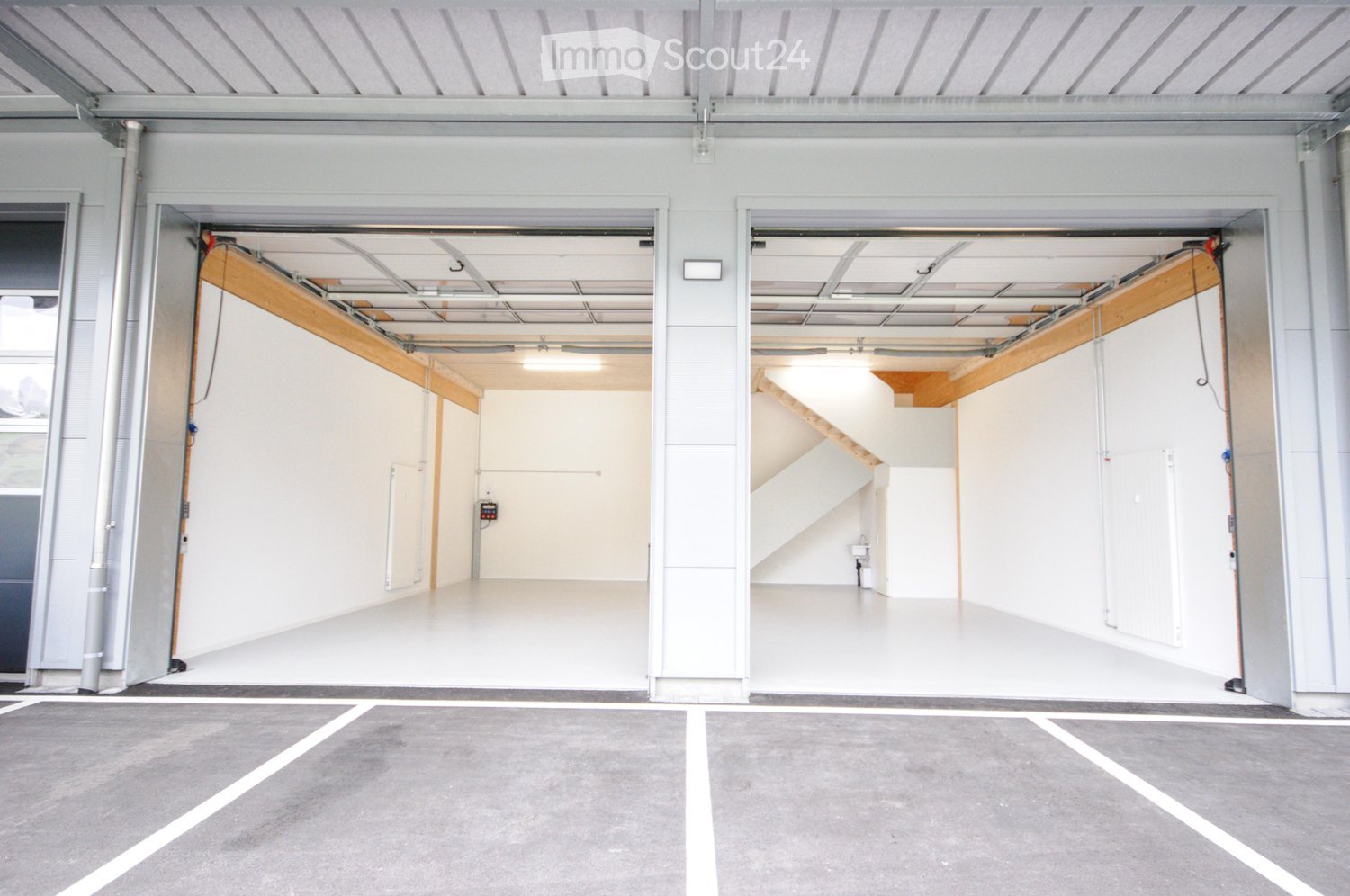 Modern, spacious garage with two large open doors, clean white interior, and a concrete parking area outside.