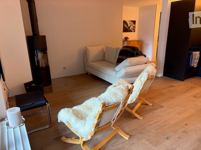 Modern living room with a white sofa, wooden floor, fireplace, and two white fur-covered chairs.