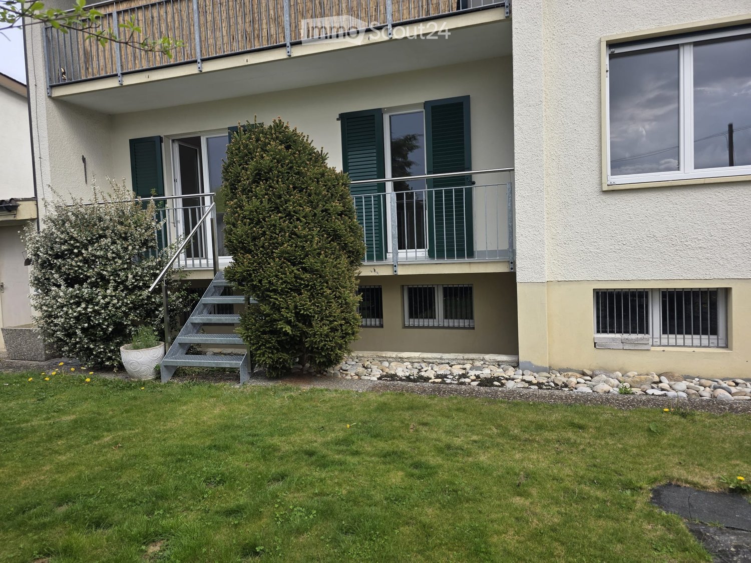 Two-story residential building with balconies, green shutters, and a well-maintained lawn in front.