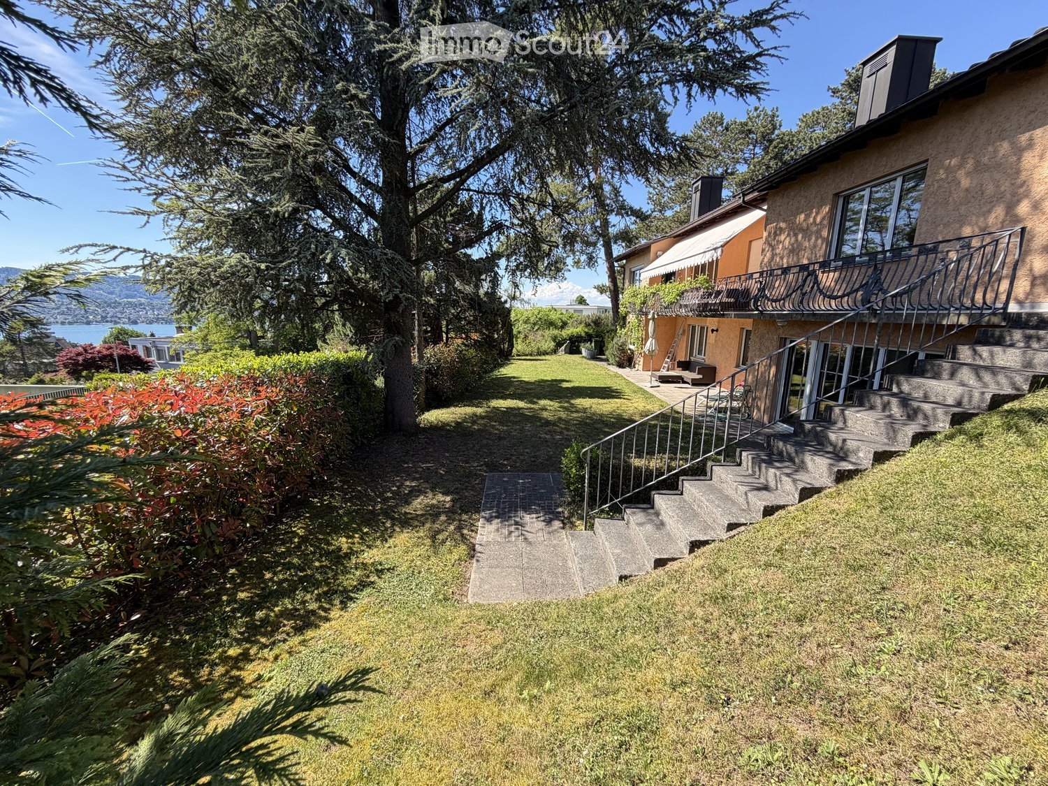 House. A two-story house with a balcony, surrounded by a well-maintained garden with a staircase leading up to the entrance.