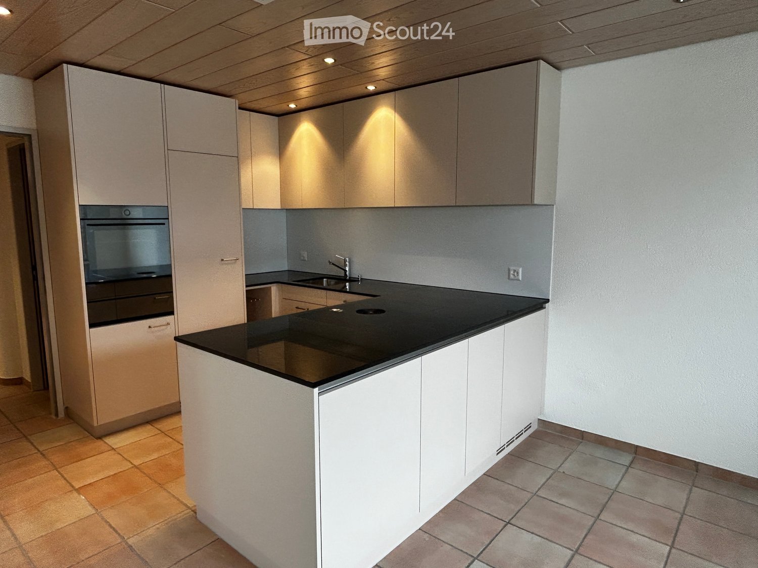 Modern kitchen with white cabinets, black countertop, built-in oven, and sink with faucet.